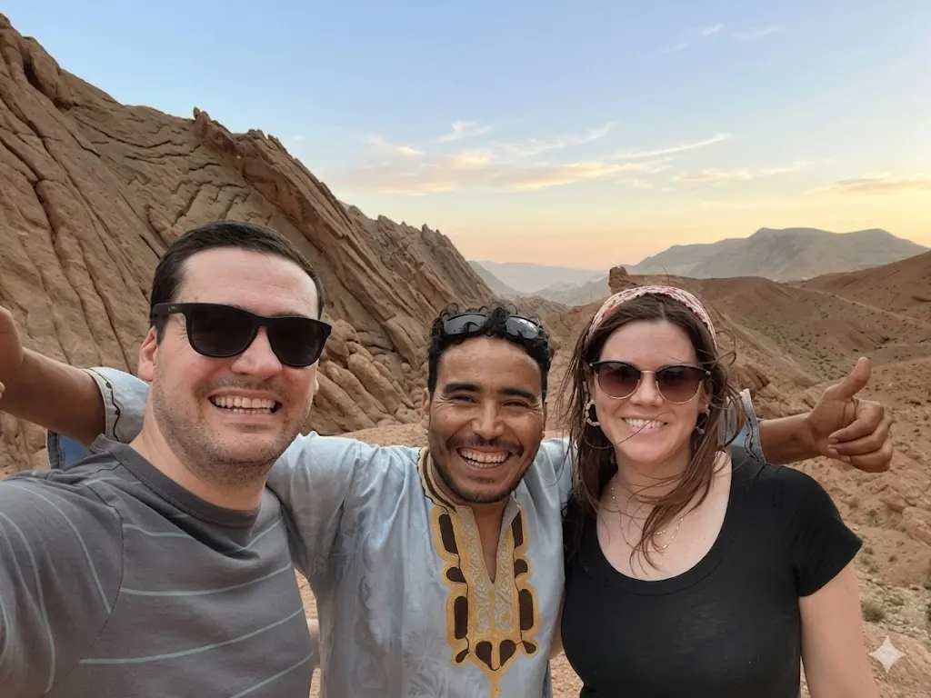 Ahmed smiling with two travellers in front of the Atlas Mountains