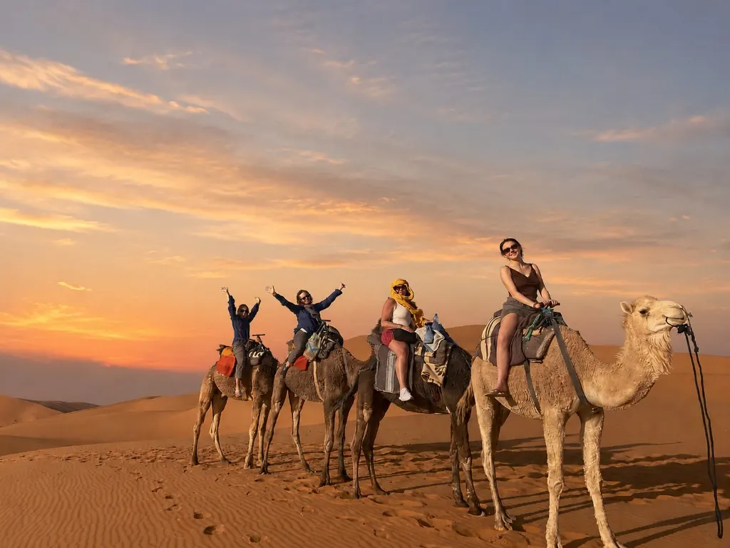 Four women riding camels across the desert at sunset