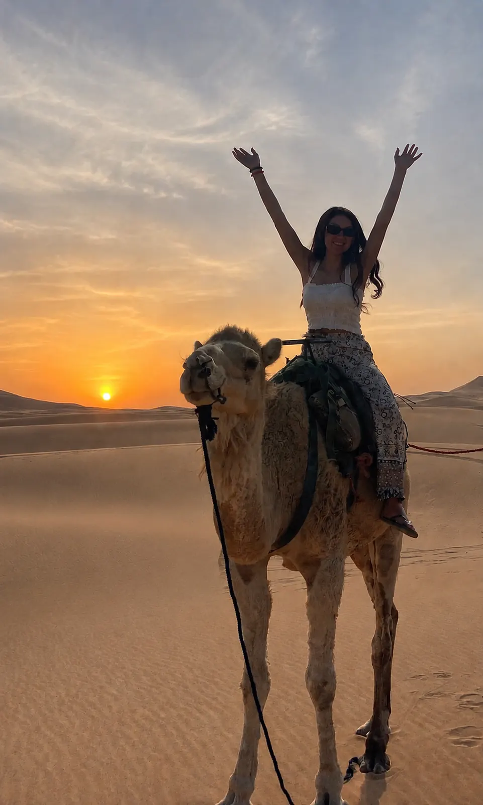 Valentina Turano riding a camel in the Sahara at sunset