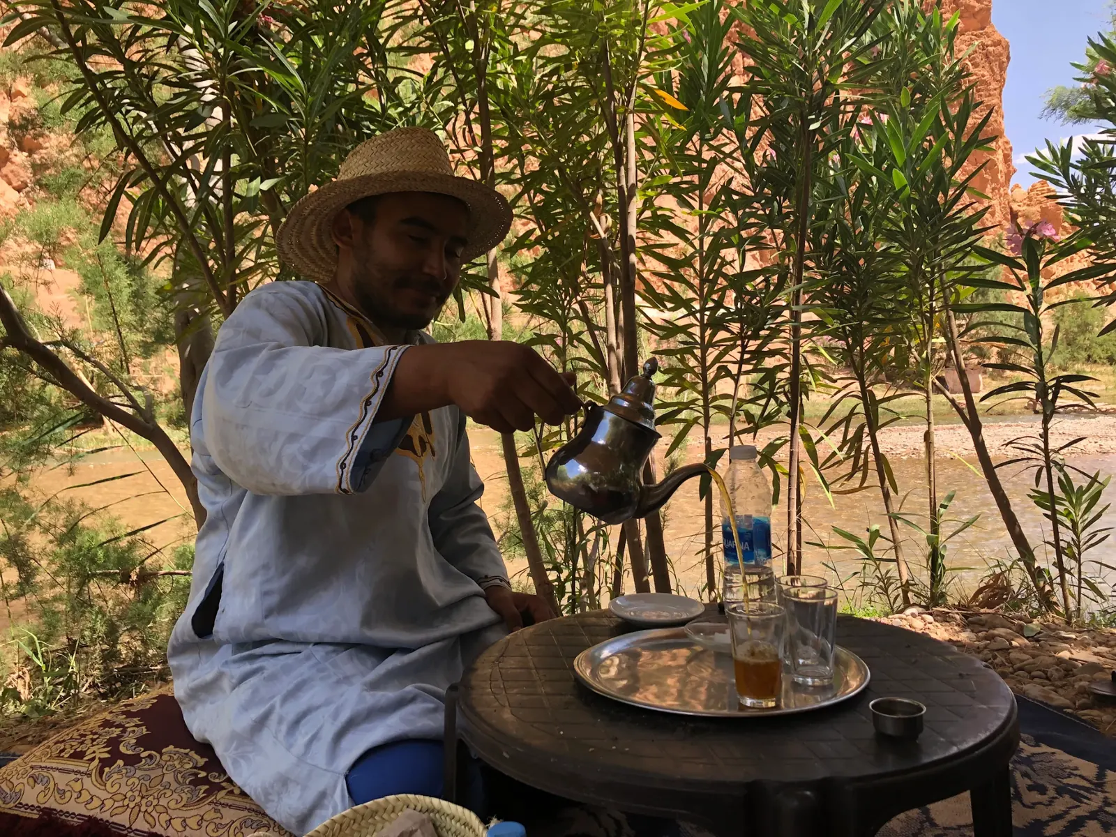 A Berber guide pouring mint tea from height beside a mountain river in the High Atlas
