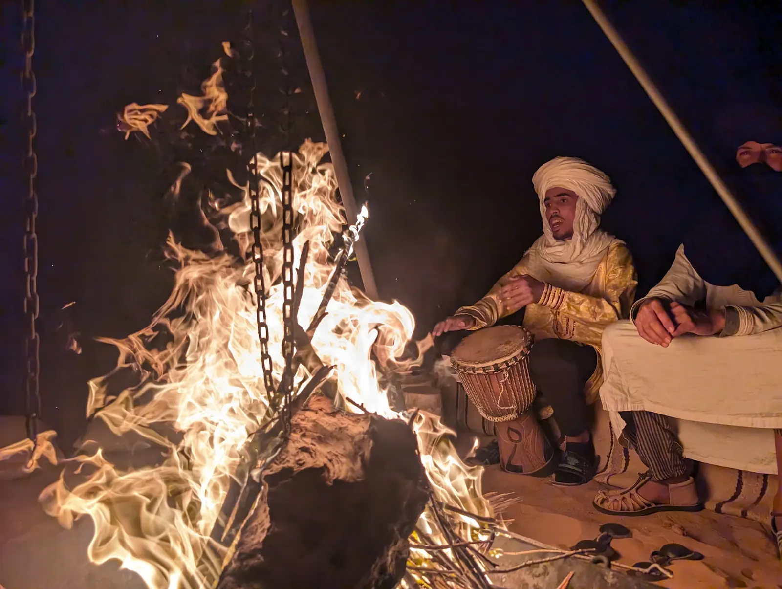 Berber musician playing drums beside a desert campfire at night