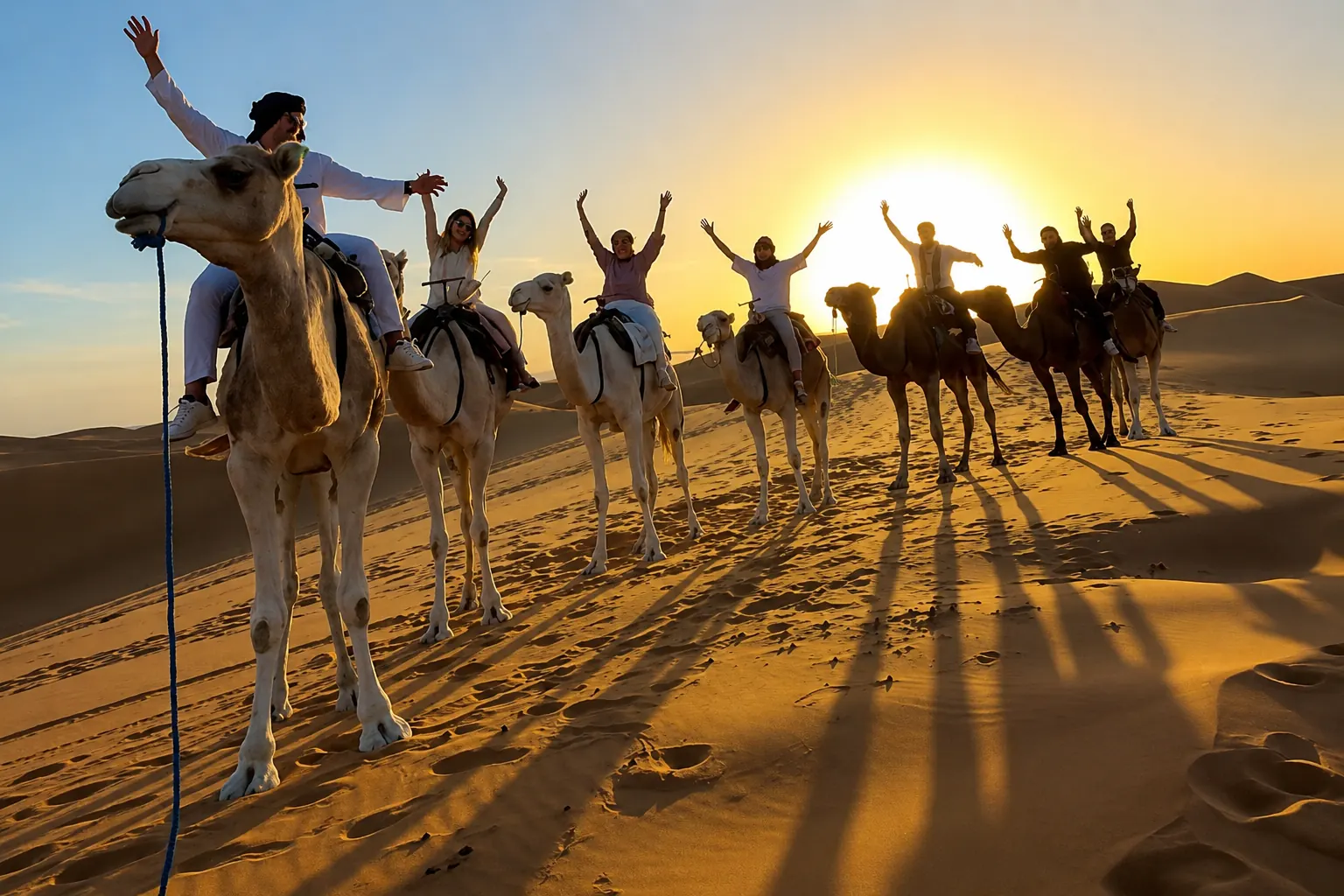 A group on a camel trek crossing the Sahara dunes at sunset