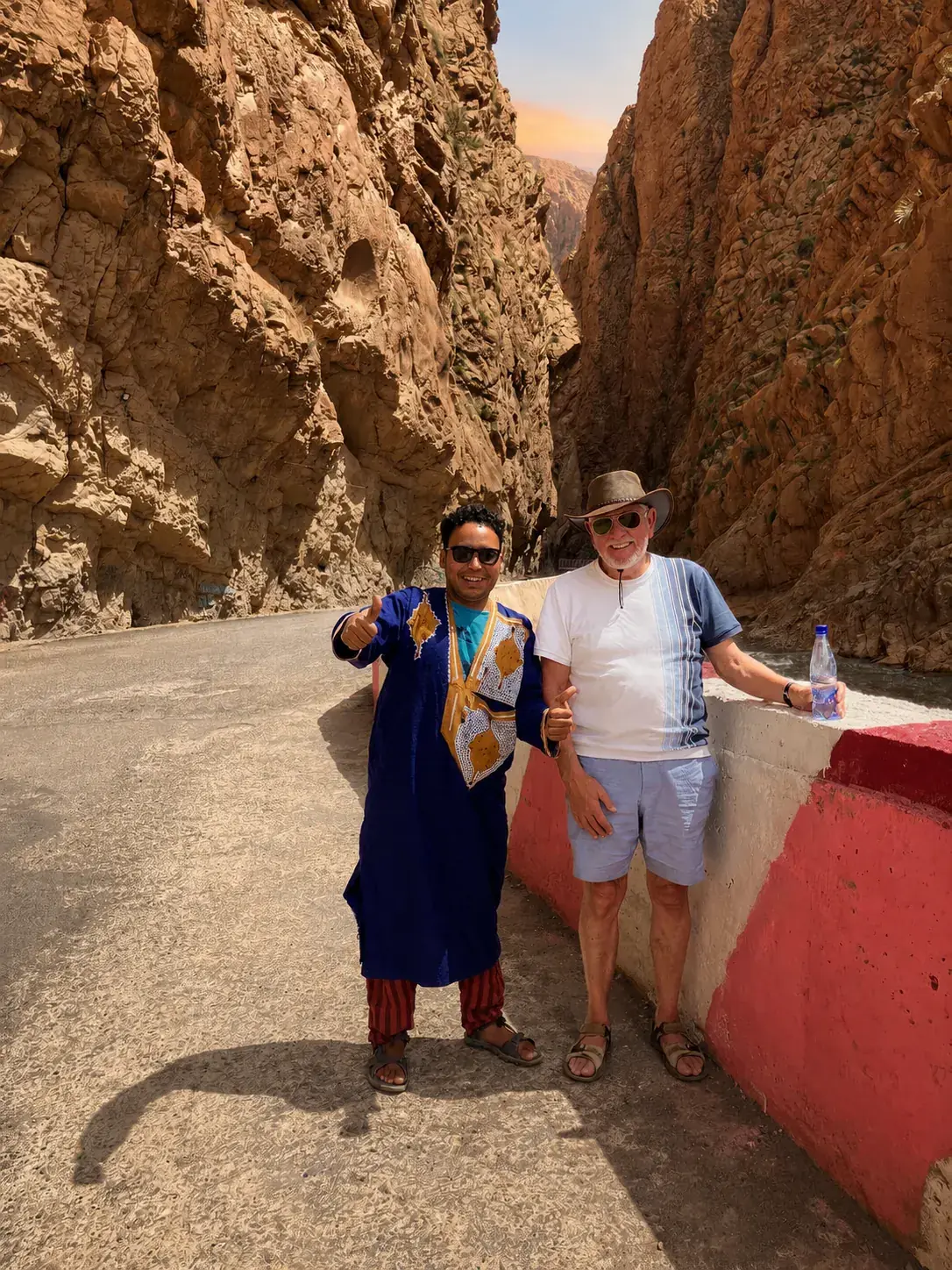 A local guide and a traveller walking between the high walls of the Todra Gorge