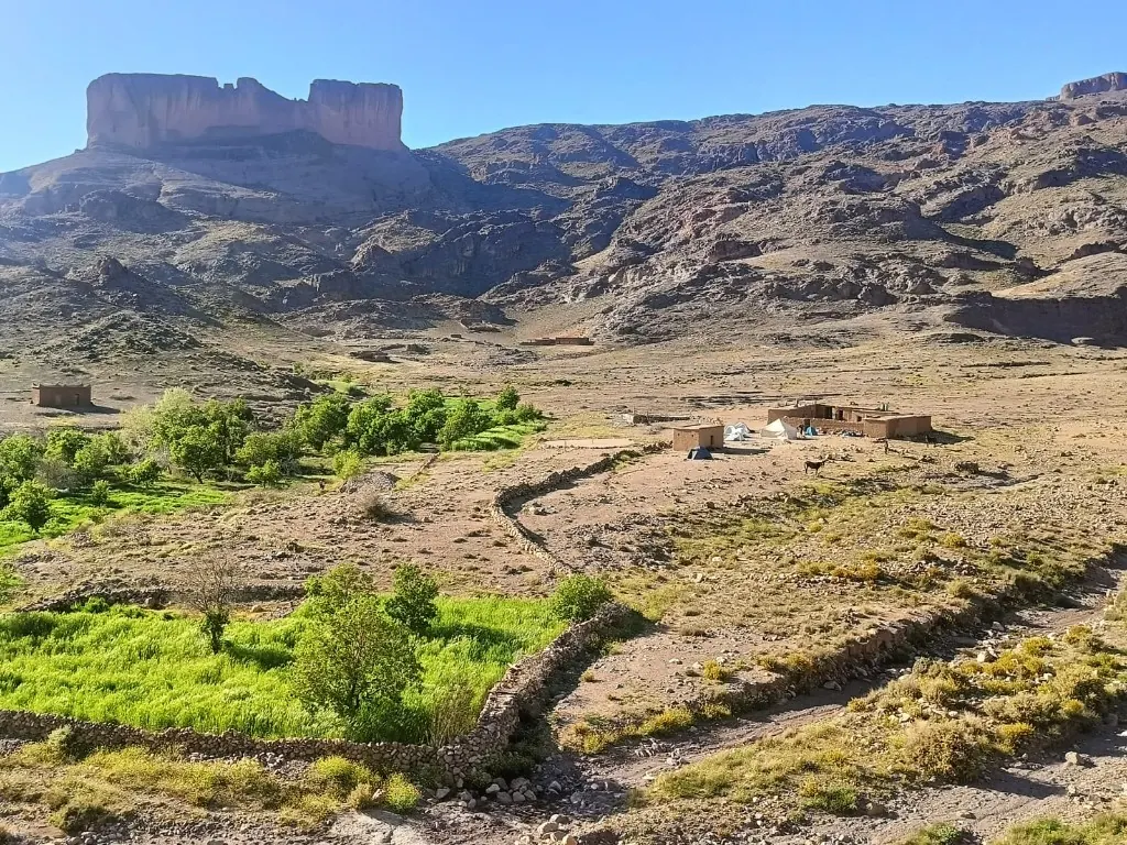 Jbel Saghro valley with green oasis fields, Berber camp and volcanic mesa beyond