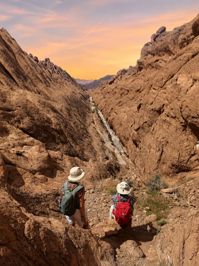 Two trekkers overlooking a deep canyon at sunset
