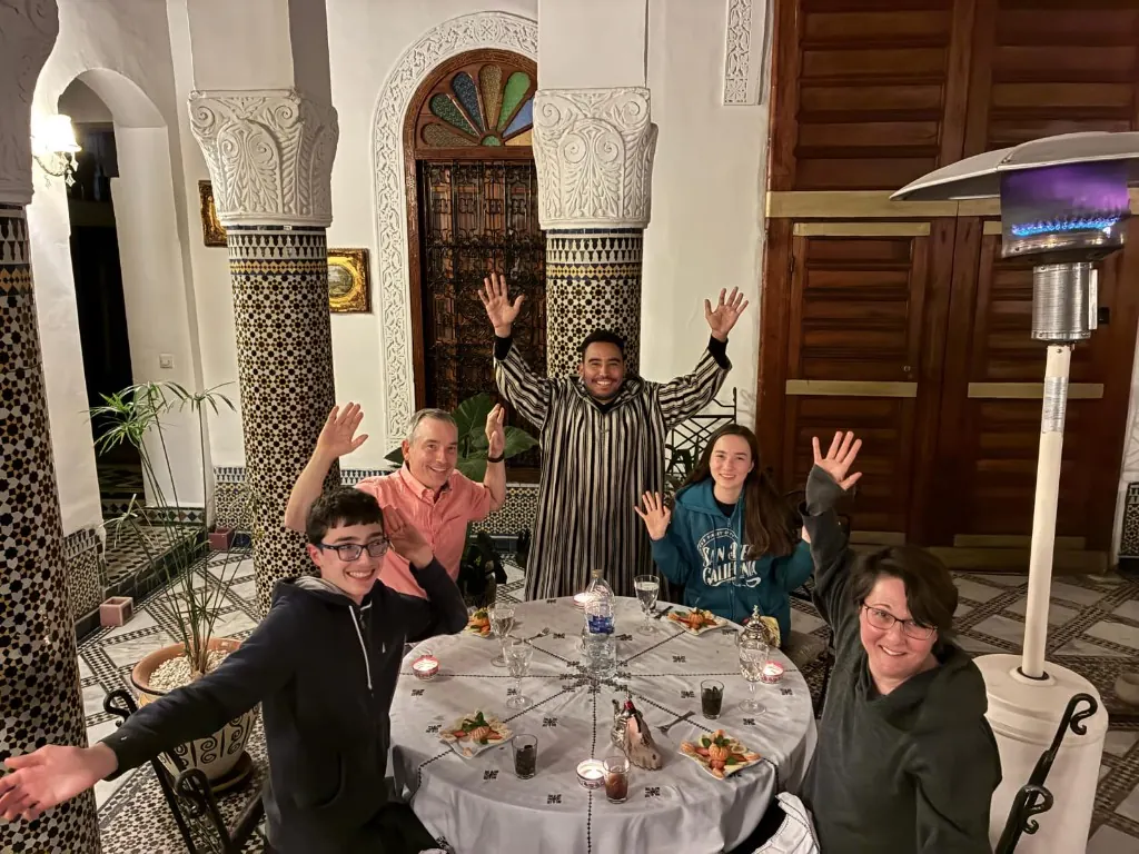 Family sharing a traditional dinner in a Moroccan riad courtyard with their host