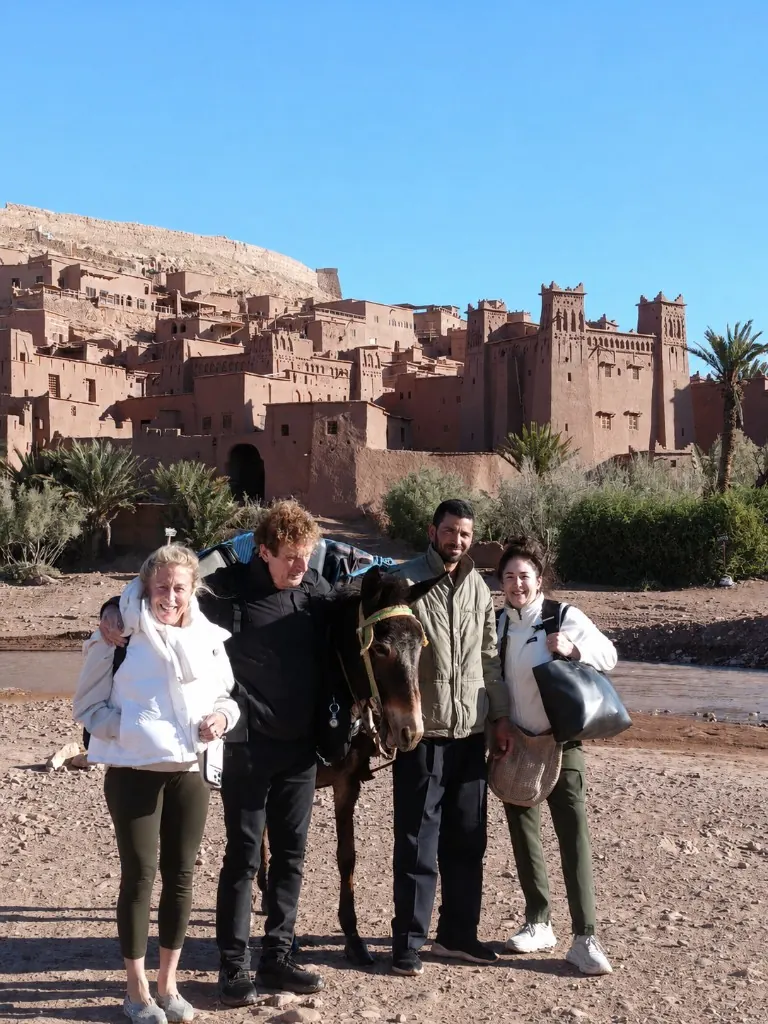 A local guide and travellers walking along the riverbed below Ait Ben Haddou with a donkey