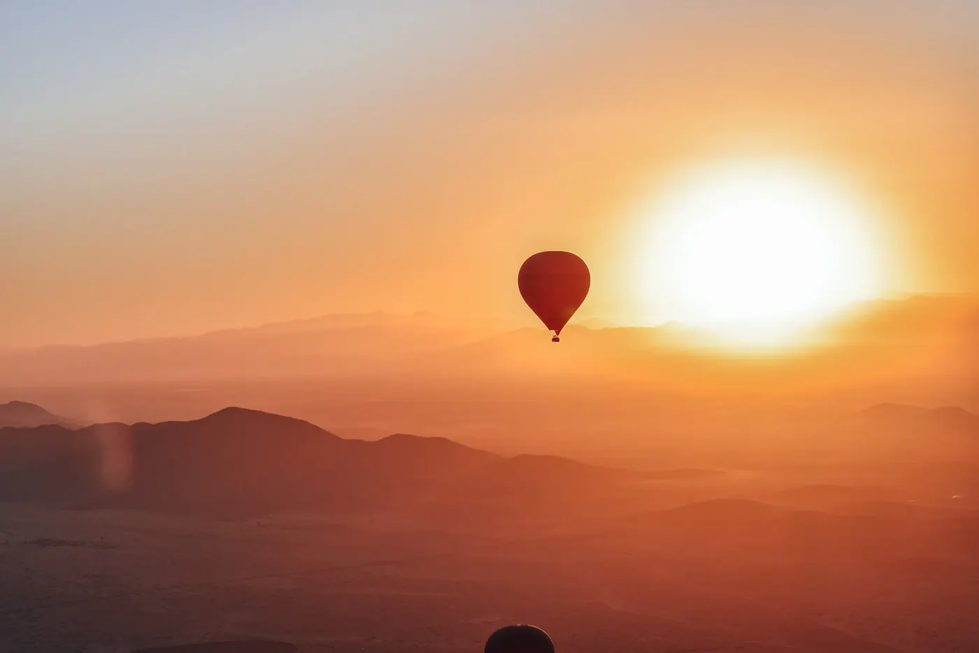 Hot air balloon silhouetted against a blazing orange sunrise over the Agafay Desert