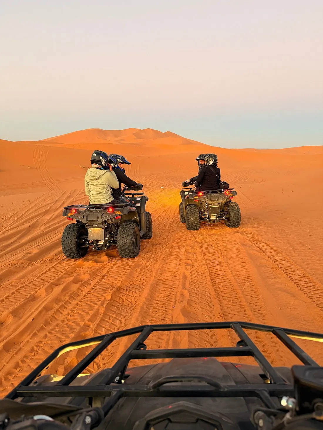 Two quad bikers riding ahead across the red Agafay Desert, POV from the saddle